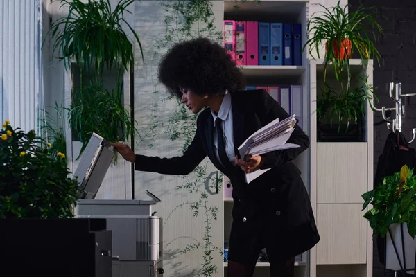 Elegant african american businesswoman with documents opening copier machine at night in office — Stock Photo