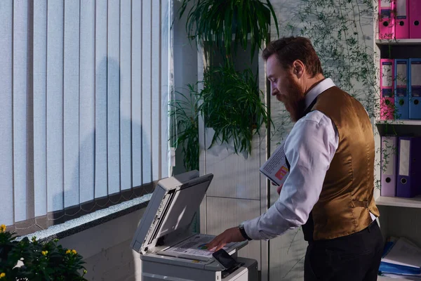 Боковой вид стильного бородатого бизнесмена в формальной одежде, ксерокопирование документов в офисе ночью — стоковое фото