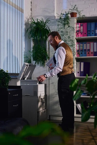 Vista laterale di barbuto elegante uomo d'affari che lavora con fotocopiatrice in ufficio in serata — Foto stock