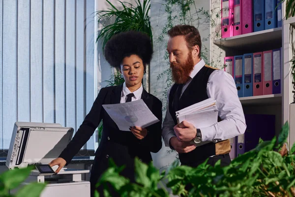 Mulher de negócios afro-americana com colega barbudo trabalhando com documentos perto de copiadora no escritório — Fotografia de Stock