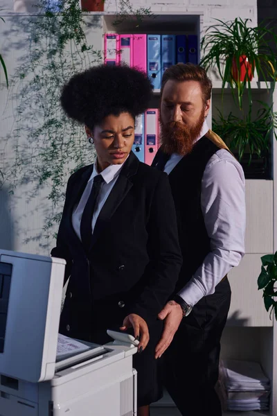Businessman seducing displeased african american woman frowning near copier in night office — Stock Photo
