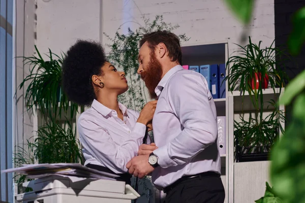 Joven afroamericano secretario desnudando barbudo hombre de negocios cerca de fotocopiadora, romance en la oficina - foto de stock
