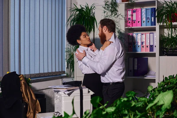 Passionate multiethnic couple hugging near copier machine in office at night, romantic encounter — Stock Photo