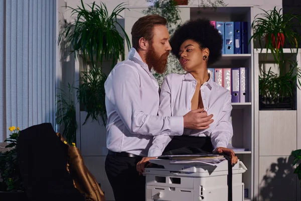 Homme d'affaires barbu séduire et déshabiller jeune secrétaire afro-américain près copieur dans le bureau — Photo de stock