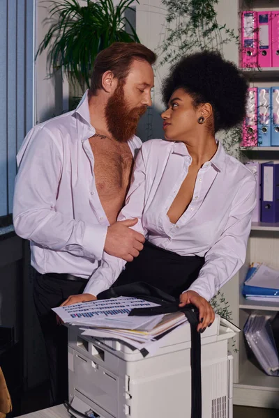 Apasionada mujer de negocios afroamericana seduciendo a un colega barbudo cerca de la fotocopiadora en el cargo — Stock Photo