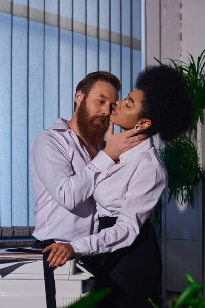 Bearded tattooed businessman hugging neck of hot african american woman near copier in office — Stock Photo