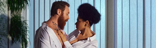 Romance de escritório, homem de negócios tatuado barbudo e mulher americana africana abraçando à noite, banner — Fotografia de Stock