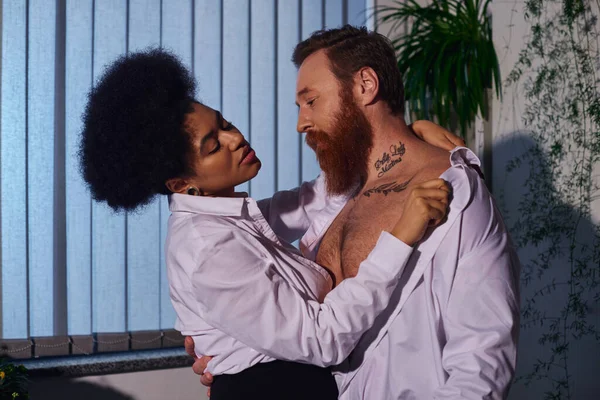 Любовний роман, гаряча афроамериканська жінка дивиться на татуйованого бородатого бізнесмена в нічному офісі — стокове фото