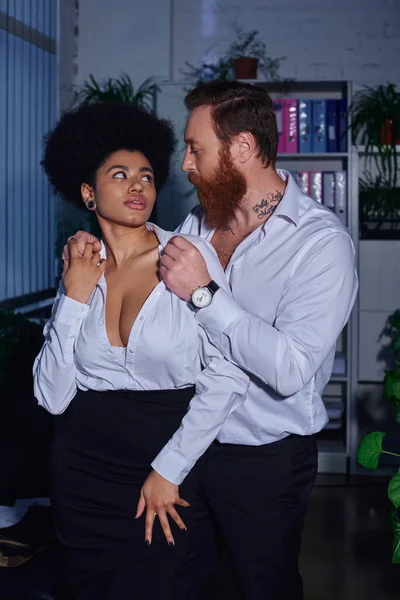 Sexy african american woman and bearded tattooed businessman looking at each other, office romance — Stock Photo
