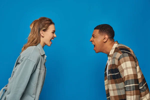 Multikulturelles Paar schreit sich vor blauem Hintergrund an, streitet und missversteht — Stockfoto