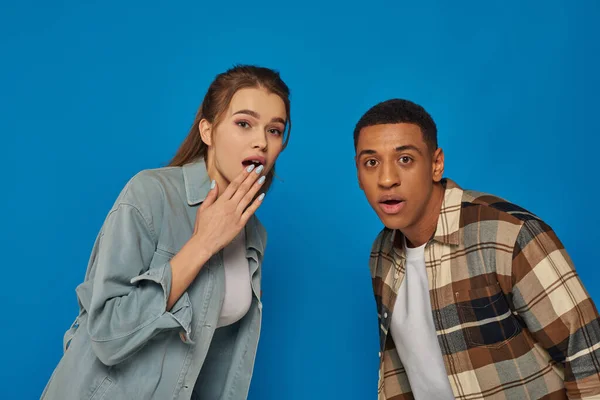 Schockierter multikultureller Mann und Frau mit offenem Mund, der in die Kamera auf blauem Hintergrund blickt, Vielfalt — Stockfoto