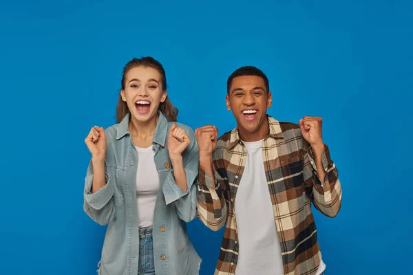 Aufgeregtes interrassisches Paar, das vor Freude in die Kamera vor blauem Hintergrund schreit, emotionale Reaktion — Stockfoto
