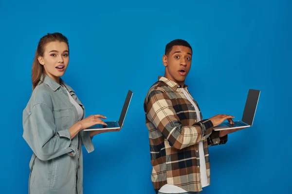 Freelancers inter-raciais espantados usando laptops em pano de fundo azul, diversas culturas homem e mulher — Fotografia de Stock