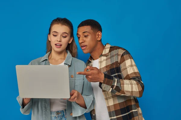 Афроамериканський чоловік вказує на ноутбук і обговорює ідеї з колегою-жінкою на синьому фоні — стокове фото