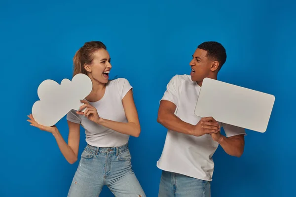 Casal interracial emocional segurando cartazes em branco no fundo azul, pensamento e bolhas de fala — Fotografia de Stock