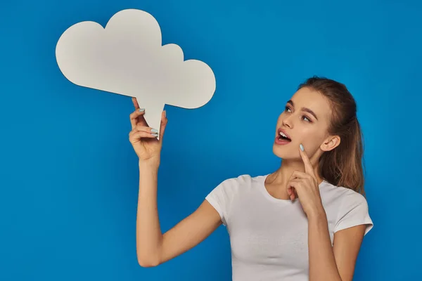 Curious young woman with open mouth looking at blank thought bubble on blue background, emotional — Stock Photo