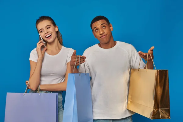 Consumismo, mulher feliz ter telefonema enquanto namorado afro-americano segurando sacos de compras — Fotografia de Stock