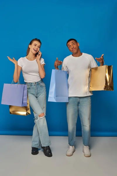 Consumismo, mulher alegre ter telefonema enquanto namorado afro-americano segurando sacos de compras — Fotografia de Stock