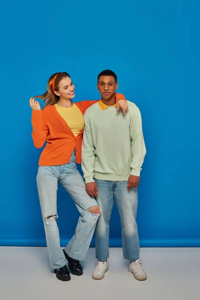 Couple interracial en tenue décontractée sur fond bleu, jeune femme étreignant homme afro-américain — Photo de stock