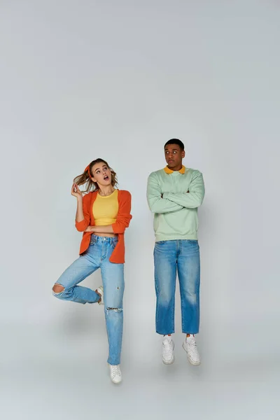 Interracial couple in casual attire jumping and looking away on grey backdrop, action shot — Stock Photo