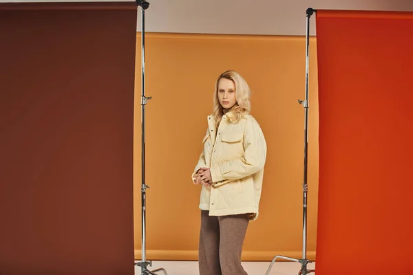 Осенняя мода, привлекательная женщина в осеннем наряде смотрит в камеру и позирует на оранжевом фоне — стоковое фото