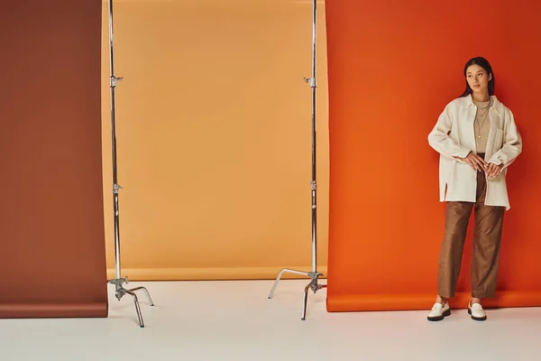 Брюнетка азіатська жінка в осінньому вбранні стоїть на різнокольоровому тлі, шкіряні штани та верхній одяг — стокове фото