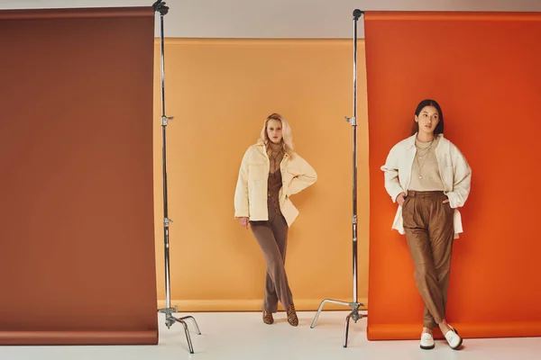 Herbstmode, junge interrassische Frauen in stilvoller Kleidung posieren vor pastellfarbener Kulisse — Stockfoto