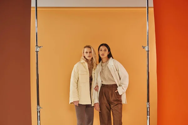 Herbstmode, junge multiethnische Frauen in stilvoller Kleidung posieren vor pastellfarbener Kulisse — Stockfoto