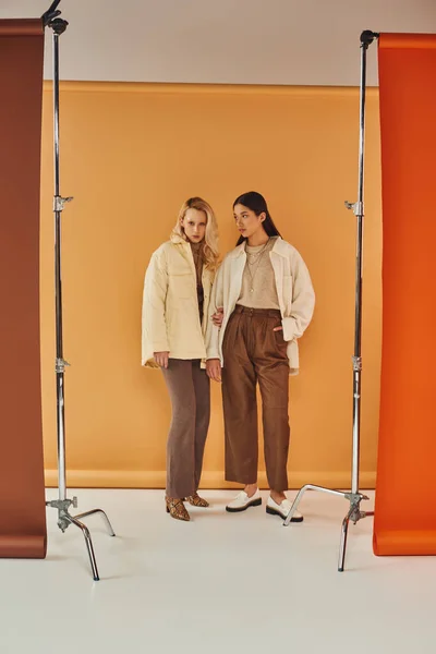 Fall fashion, young and stylish women in autumn attire posing on pastel multicolored backdrop — Stock Photo