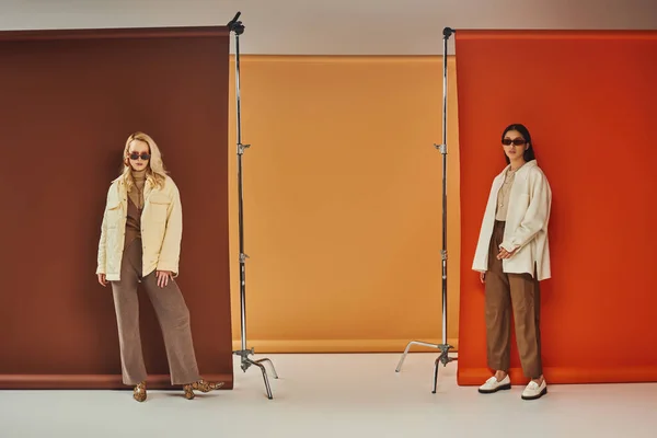Mode d'automne, modèles multiethniques élégants dans les lunettes de soleil et les vêtements de dessus posant sur fond coloré — Photo de stock