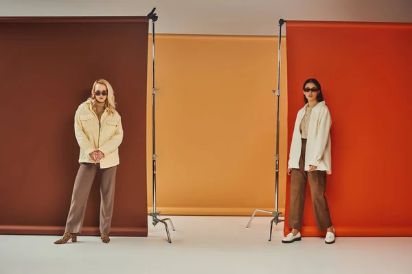 Herbstmode, stylische multiethnische Models in Sonnenbrille und Oberbekleidung posieren vor buntem Hintergrund — Stockfoto