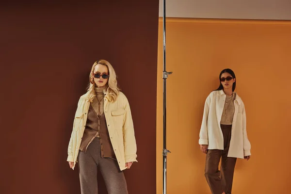 Осенний гардероб, стильные мультиэтнические женщины в солнцезащитных очках и верхней одежде позируют на красочном фоне — стоковое фото