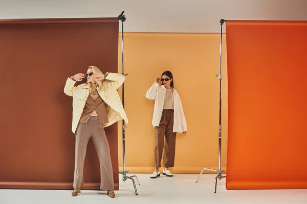 Automne, modèles multiethniques en lunettes de soleil et vêtements d'extérieur d'automne posant sur fond coloré — Photo de stock
