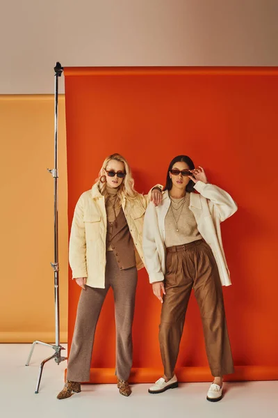 Moda e estilo, modelos multiétnicos em óculos de sol e outerwear posando em estúdio, cores de outono — Fotografia de Stock