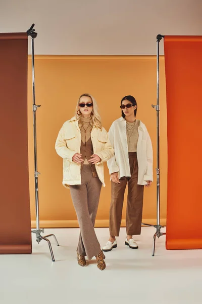 Modelli interrazziali in occhiali da sole e capispalla autunno in posa in studio, colori autunnali, duo sullo sfondo — Foto stock
