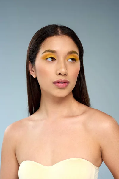Asiatisches Model mit brünetten Haaren und fettem Make-up, das isoliert von blauer, vielfältiger Schönheit wegschaut — Stockfoto