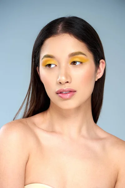 Weibliche Sinnlichkeit, junges asiatisches Model mit kühnem Make-up und nackten Schultern posiert vor blauem Hintergrund — Stockfoto