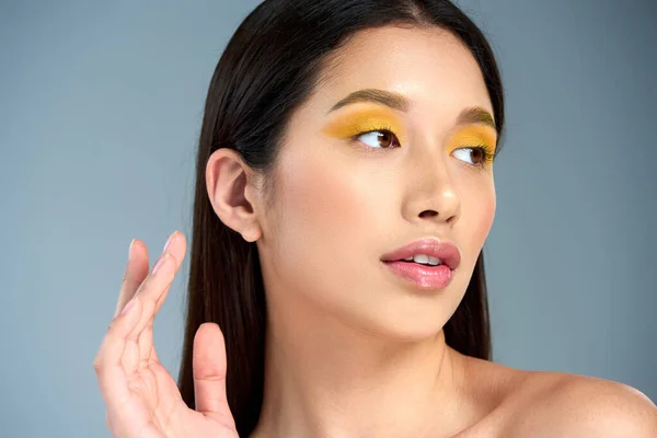 Elegance, asian woman with bold makeup and bare shoulders looking away and posing on blue backdrop — Stock Photo