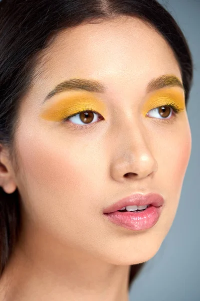 Schönheit und Jugend, asiatische Frau mit kühnem Make-up, die vor blauem Hintergrund wegschaut, Porträt aus nächster Nähe — Stockfoto