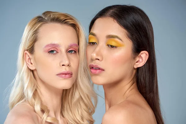 Verschiedene Schönheit, Porträt von zwei interrassischen Frauen mit kühnem Make-up posiert auf blauem Hintergrund — Stockfoto