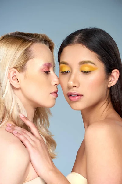 Verschiedene Schönheit, Porträt zweier multiethnischer Models mit kühnem Augen-Make-up auf blauem Hintergrund — Stockfoto