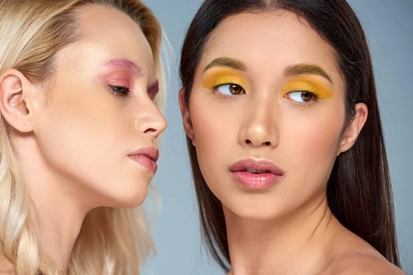 Vielfältige Schönheit, Porträt zweier multikultureller Models mit kühnem Make-up auf blauem Hintergrund — Stockfoto