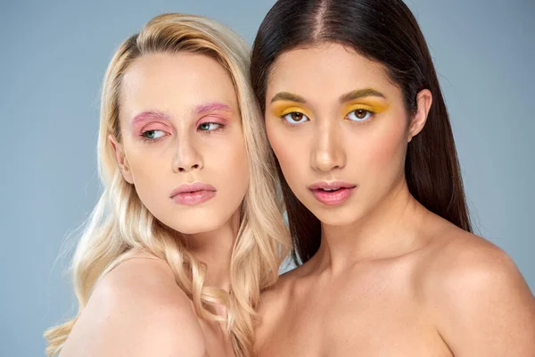 Vielfältige Schönheit, Porträt zweier multikultureller Models mit lebendigem Make-up auf blauem Hintergrund — Stockfoto