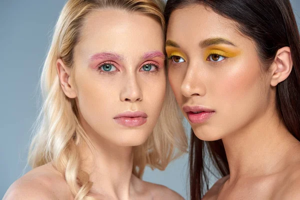 Vielfältiges Schönheitskonzept, interrassische Frauen mit kühnem Augen-Make-up posieren auf blauem Hintergrund, feminin — Stockfoto