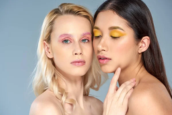 Concepto de belleza diversa, modelos multiétnicos con maquillaje de ojos en negrita mirando a la cámara en el fondo azul - foto de stock