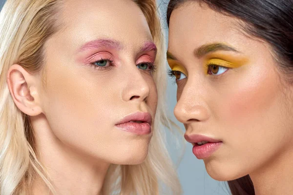 Vielfältiges Schönheitskonzept, multiethnische Frauen mit lebendigem Augen-Make-up posieren gemeinsam vor blauem Hintergrund — Stockfoto