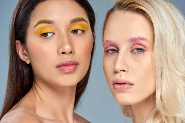 Multikulturelle Frauen mit lebendigem Augen-Make-up posieren gemeinsam vor blauem Hintergrund, ausdrucksstarke Augen — Stockfoto