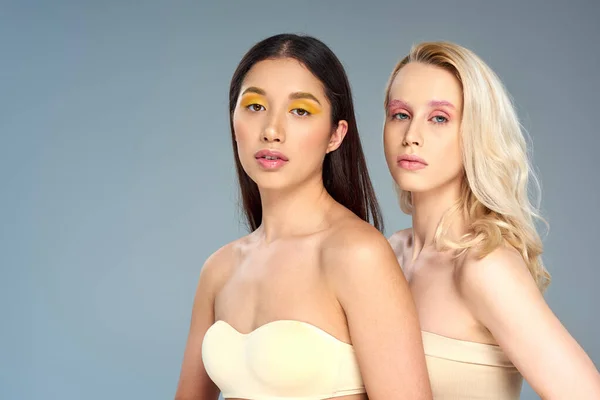 Modelos jóvenes multiétnicos con maquillaje de ojos audaces posando juntos sobre el telón de fondo azul, concepto de tendencia de belleza - foto de stock