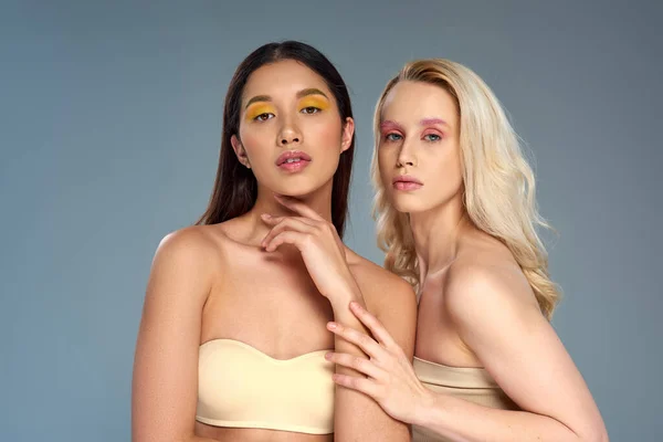 Models mit kühnem Augen-Make-up posieren in Unterwäsche vor blauem Hintergrund, vielfältiges Schönheitskonzept — Stockfoto