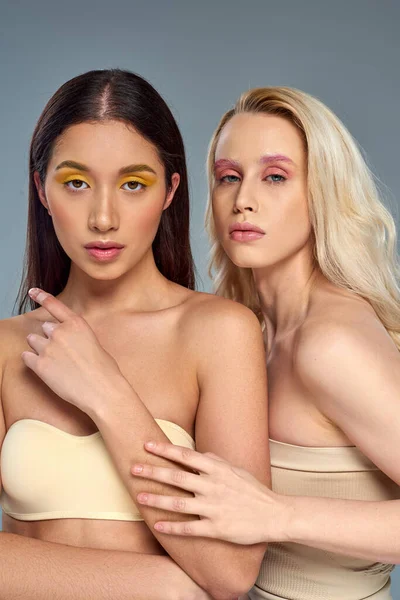 Multiethnische Models mit kühnem Augen-Make-up posieren in Unterwäsche vor blauem Hintergrund, vielfältiges Schönheitskonzept — Stockfoto